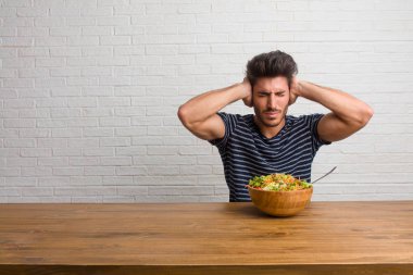 Eller, kızgın ve bazı ses işitme yorgun kulaklarıyla kapsayan bir masada oturan genç yakışıklı ve doğal adam. Taze bir salata yemek.