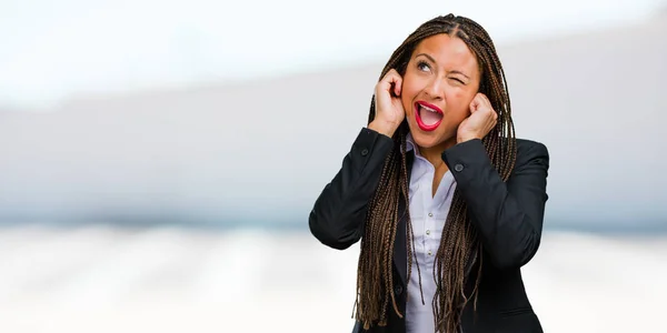 Portrait of a young black business woman covering ears with hands, angry and tired of hearing some sound