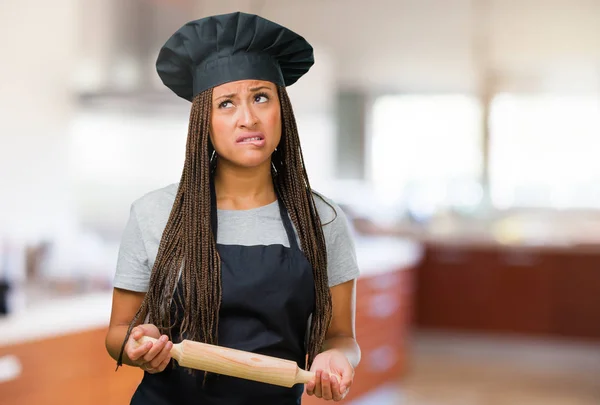 Young black woman in baker hat doubting and confused, thinking of an idea or worried about something