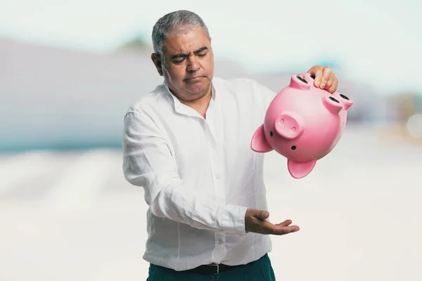 Middle aged man sad and disappointed, holding a piglet bank, no money left, trying to get something out