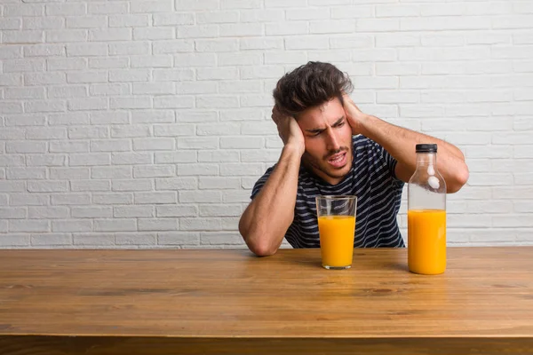 Young handsome and natural man sitting on a table frustrated and desperate, angry and sad with hands on head. Having a breakfast, includes orange juice and a cereals bowl.