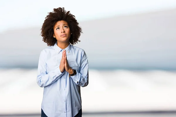 young black woman in blue shirt praying on blurred background