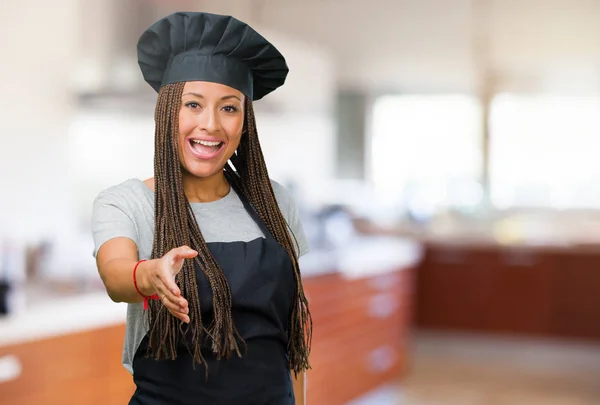 Portrait of a young black baker woman reaching out to greet someone or gesturing to help, happy and excited