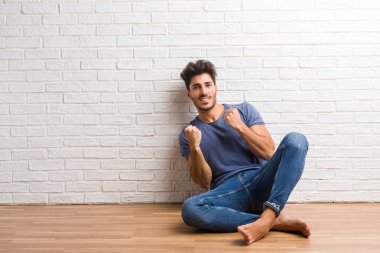 Doğal delikanlı oturup bir ahşap zemin üzerinde çok mutlu ve heyecanlı, silah, bir zafer ya da başarı, piyango kazanan kutluyor yetiştirme