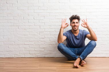 Doğal delikanlı oturup bir ahşap zemin üzerinde neşeli ve kendine güvenen heyecanlı ve çığlık, onay ve başarı kavramı ok jest yapıyor