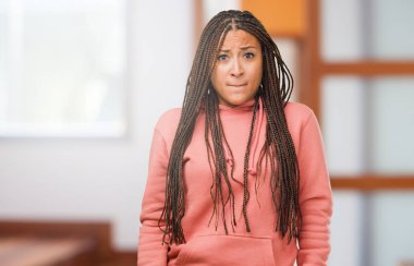 Portrait of a young black woman wearing braids doubting and confused, thinking of an idea or worried about something clipart