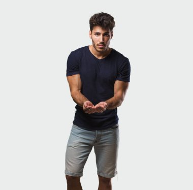 Genç yakışıklı ayakta el ile bir şey tutan adam bir ürün, gülümseyen ve neşeli gösterilen, hayali bir nesne sunan