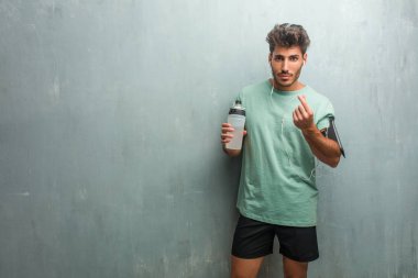 Genç fitness adamla bir kol bandı ile telefon giyen ihtiyaç, bir jest yapma spor şişe bir grunge duvara üzgün ve depresyonda,.