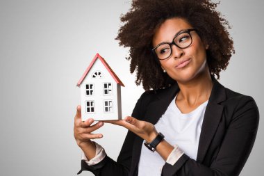 gri arka plan üzerinde küçük bir ev tutarak siyah iş kadını