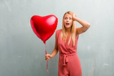 Zarif sarışın genç kadın sinirli ve umutsuz, kızgın ve üzgün ile portresi ellerinizi başınızın koyun. Bir kırmızı kalp balon holding.