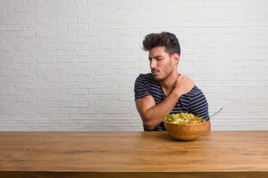 Sırt ağrısı nedeniyle iş stresi, yorgun ve zeki bir masada oturan genç yakışıklı ve doğal adam. Taze bir salata yemek.