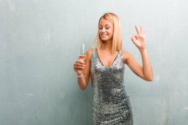 Zarif sarışın genç kadın neşeli ve kendine güvenen yapıyor Tamam jest, heyecanlı ve çığlık, kavram onayı ve başarı portresi. Bir şampanya kadehi holding.