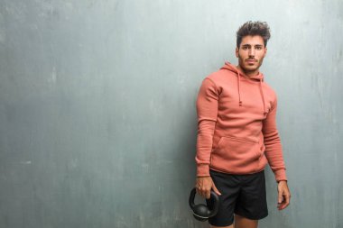 Bir demir dumbbell tutarak genç fitness adam ile kalça, ellerinde bir grunge duvara.