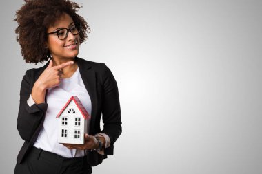 gri arka plan üzerinde küçük bir ev tutarak siyah iş kadını