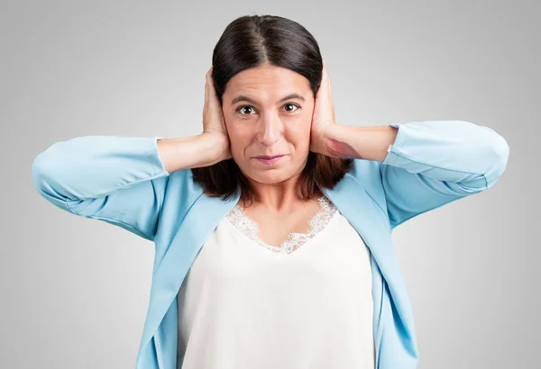 Middle aged woman covering ears with hands, angry and tired of hearing some sound