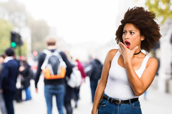 surprised young black woman covering her mouth on blurred background