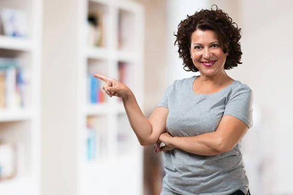 Middle aged woman pointing to the side, smiling surprised presenting something, natural and casual