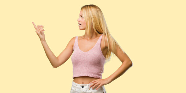 Портрет молодой красивой блондинки, указывающей в сторону, улыбающейся удивленной, представляющей что-то естественное и случайное
