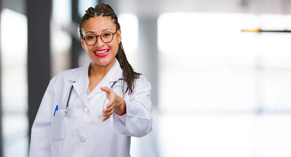 Portrait of a young black doctor woman reaching out to greet someone or gesturing to help, happy and excited