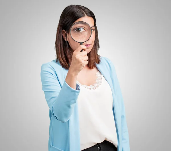 Middle aged woman surprised and wide-eyed looking through a magnifying glass, studying something, finding evidence