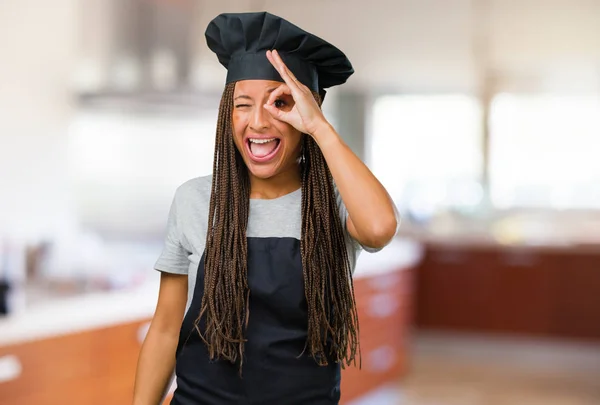 Portrait of a young black baker woman cheerful and confident doing ok gesture, excited and screaming, concept of approval and success