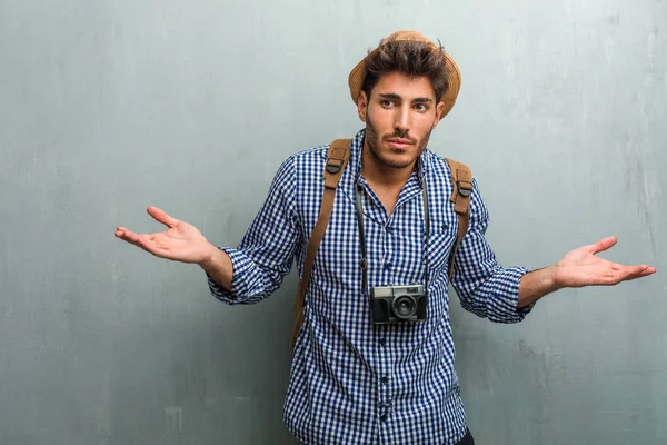 年轻英俊的旅行男子戴着草帽 背包和照相相机怀疑和耸耸肩的肩膀 优柔寡断和不安全感的概念 不确定的东西 — 图库照片