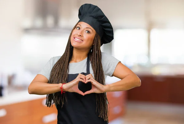 Portrait of a young black baker woman making a heart with hands, expressing the concept of love and friendship, happy and smiling