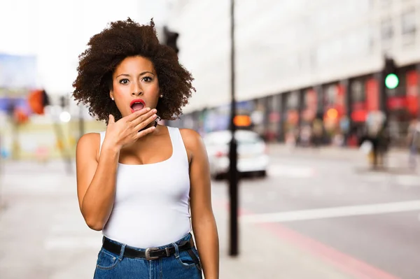 surprised young black woman covering her mouth on blurred background