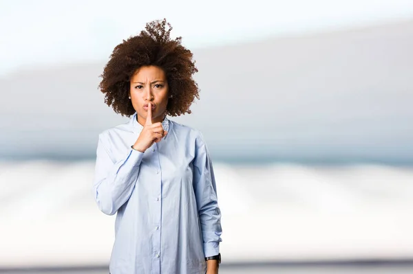 young black woman in blue shirt doing silence gesture on blurred background