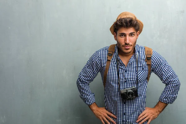 Young handsome traveler man wearing a straw hat, a backpack and a photo camera very angry and upset, very tense, screaming furious, negative and crazy