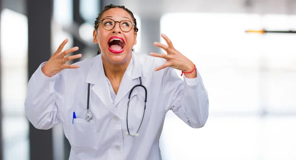 Portrait of a young black doctor woman very angry and upset, very tense, screaming furious, negative and crazy