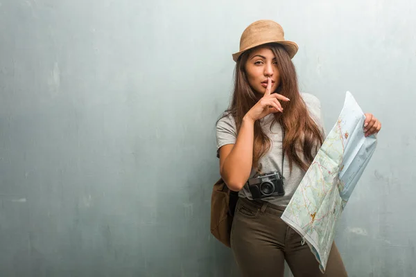 Portrait of young traveler latin woman against a wall keeping a secret or asking for silence, serious face, obedience concept. Holding a city map.