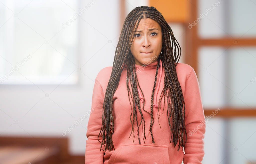 Portrait of a young black woman wearing braids doubting and confused, thinking of an idea or worried about something