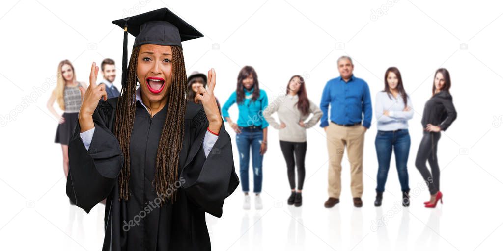 Young graduated black woman wearing braids crossing his fingers, wishes to be lucky for future projects, excited but worried, nervous expression closing eyes