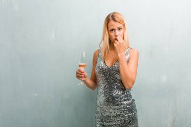 Isırma zarif sarışın genç kadın portresi çivi, gergin ve çok endişeli ve gelecek için korkmuş panik ve stres hissediyor. Bir şampanya kadehi holding.