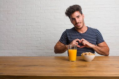 Sevgi ve dostluk, mutlu ve gülümseyerek kavramı ifade bir kalp el ile yapma bir masada oturan genç yakışıklı ve doğal bir adam. Bir kahvaltı yapıyor, portakal suyu ve tahıl bowl içerir.