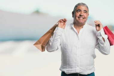 Orta yaşlı adam neşeli ve gülümseyen, alışveriş çantaları taşırken çok heyecanlı alışverişe gitmek ve yeni tekliflere bak hazır