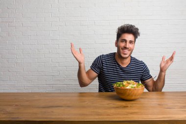 Rahat ve neşeli, gülen ve having fun, bir masada oturan genç yakışıklı ve doğal adam kendinden emin ve başarılı hisseder. Taze bir salata yemek.