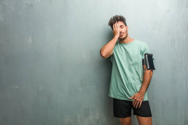 Young fitness man against a grunge wall worried and overwhelmed, wearing an armband with phone.