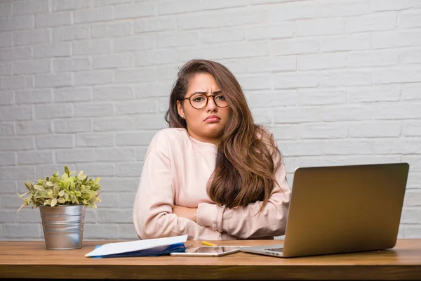 Şüphe ve omuzlarında shrugging masada oturan genç öğrenci latin kadın portresi