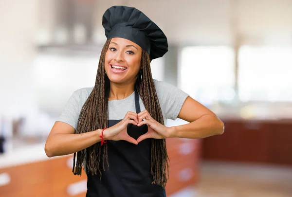 Portrait of a young black baker woman making a heart with hands, expressing the concept of love and friendship, happy and smiling