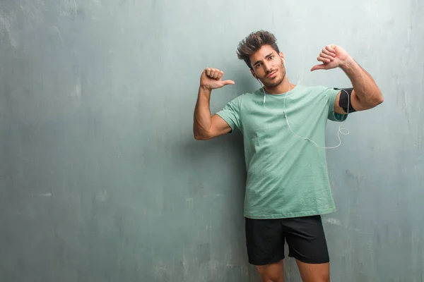 Young fitness man against a grunge wall proud and confident, pointing fingers, wearing an armband with phone.