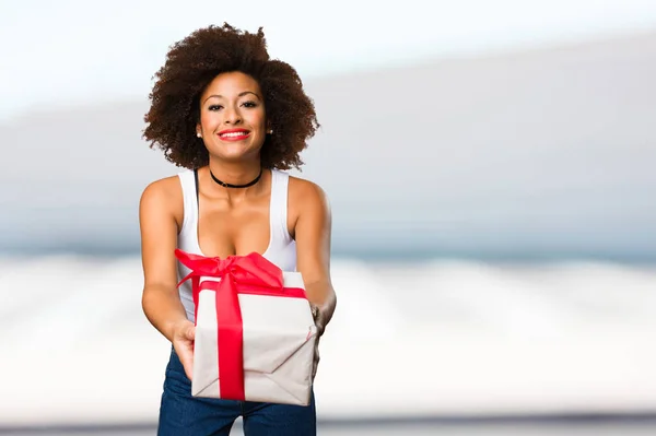 young black woman holding a gift with red ribbon on blurred background
