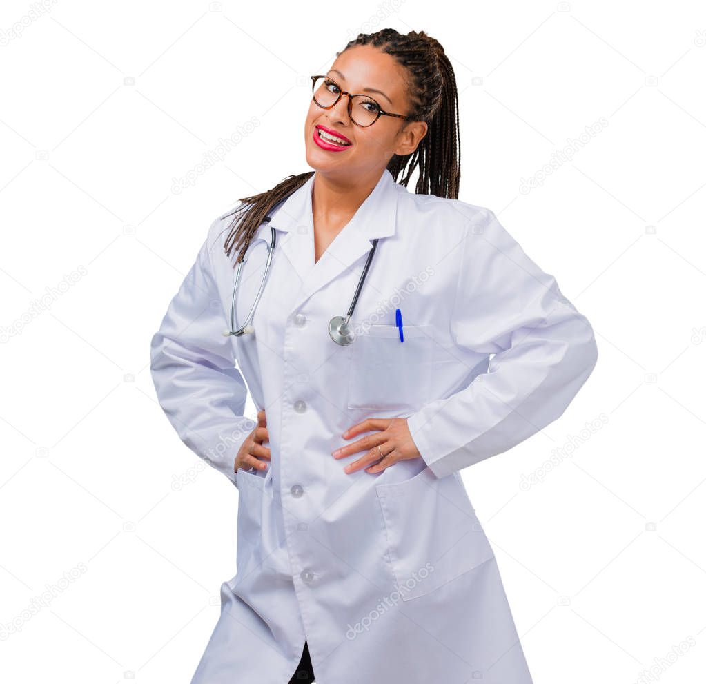 Portrait of a young black doctor woman with hands on hips, standing, relaxed and smiling, very positive and cheerful