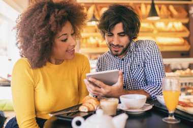 Genç çift bir fırın olarak serin bir kahvaltı ve tablet kullanma. Eğleniyor ve gülümseyen.