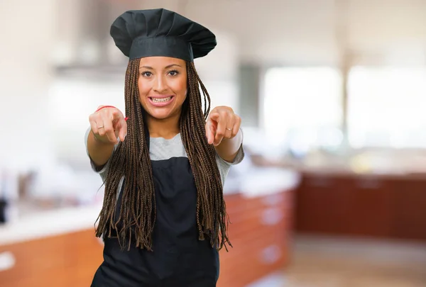 Portrait of a young black baker woman cheerful and smiling pointing to the front