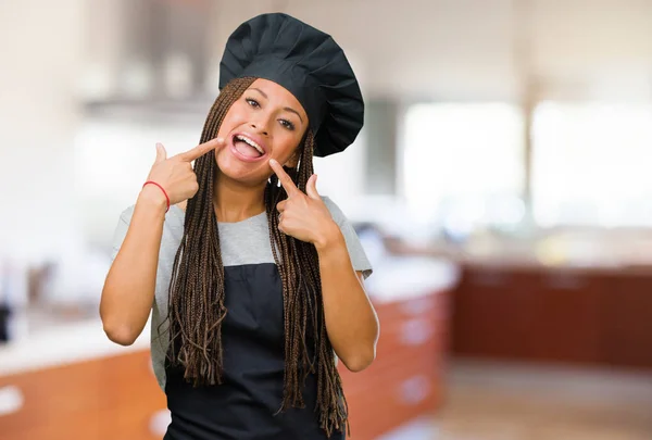 Portrait of a young black baker woman smiles, pointing mouth, concept of perfect teeth, white teeth, has a cheerful and jovial attitude
