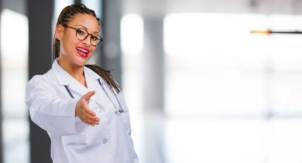 Portrait of a young black doctor woman reaching out to greet someone or gesturing to help, happy and excited