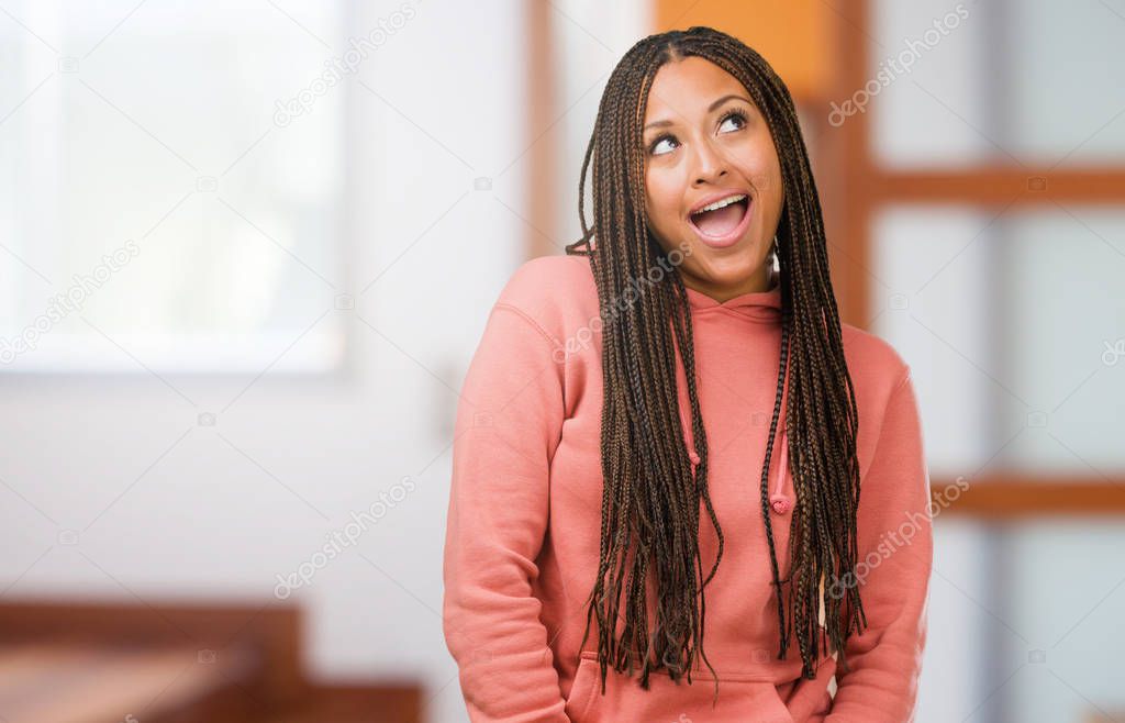 Portrait of a young black woman wearing braids looking up, thinking of something fun and having an idea, concept of imagination, happy and excited