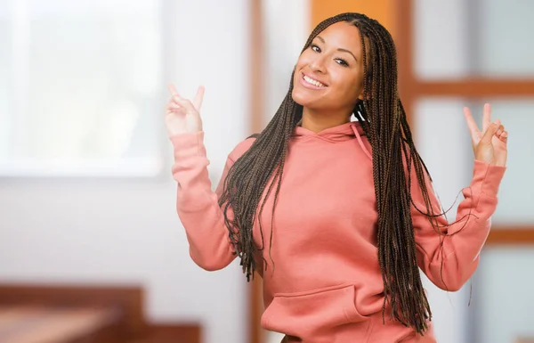 Portrait of a young black woman wearing braids fun and happy, positive and natural, makes a gesture of victory, peace concept